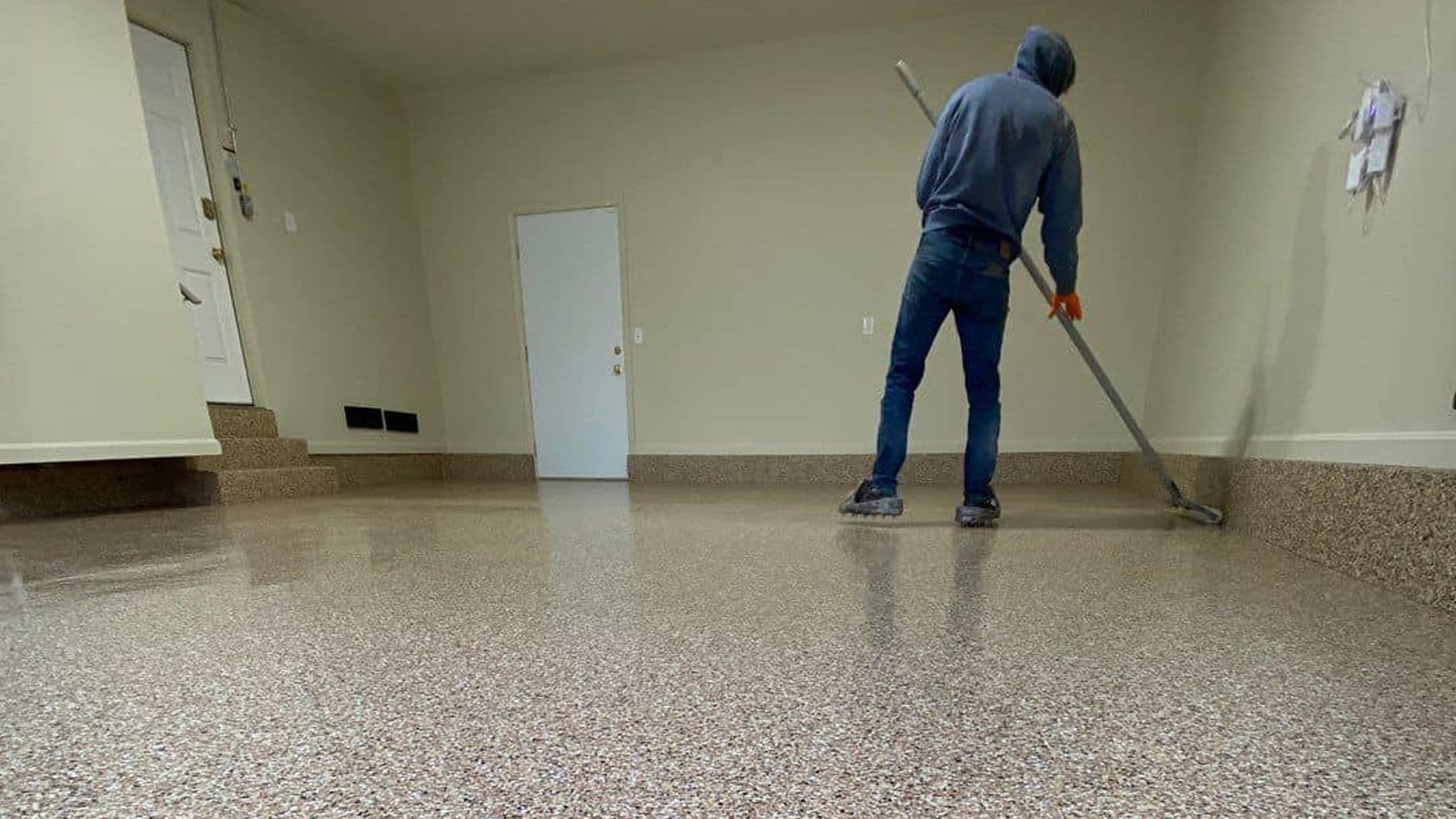 Technician applying a polyaspartic garage floor coating, featured in Sullivan's Concrete Coatings' guide on why polyaspartic is better than epoxy